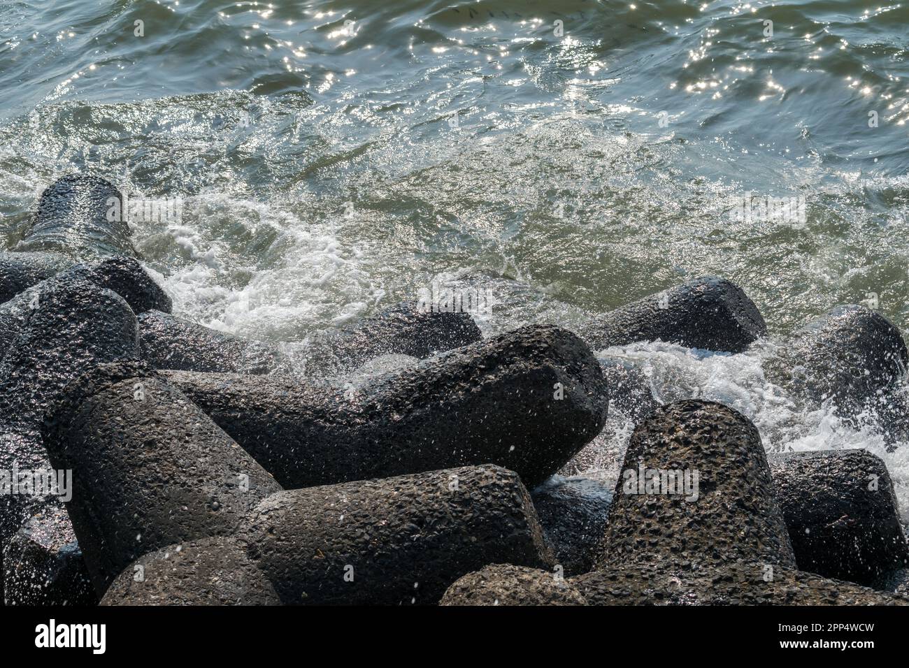 An einem sonnigen Tag in Mumbai, Indien, stürzen die blauen Wellen an der Küste mit Sprühnebel und Schaum auf Felsen Stockfoto