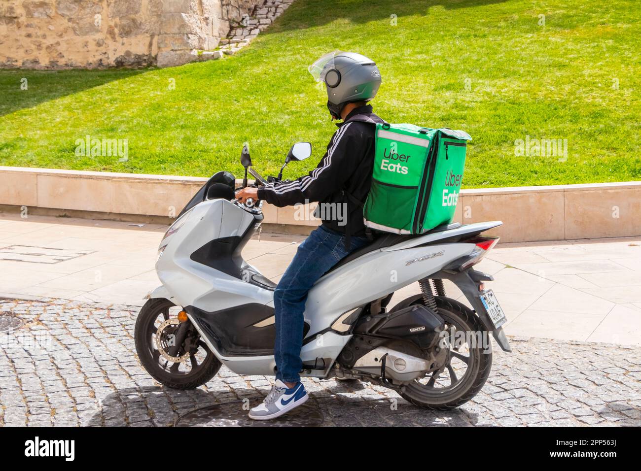 Ein junger Mann auf einem Moped-Roller, der für Uber liefert, isst in loule portugal Lebensmittel Stockfoto
