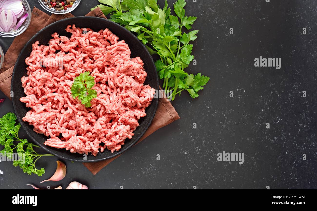 Rohes Rinderhackfleisch auf einem Teller auf schwarzem Steinhintergrund mit Kopierbereich. Draufsicht, flach liegend Stockfoto