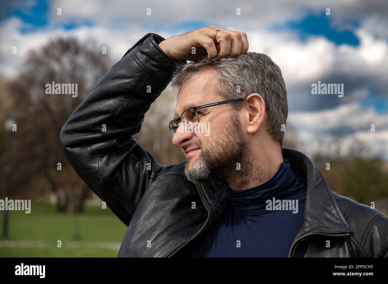 Ein 50-jähriger Mann in der schwarzen Lederjacke kratzt sich den Kopf, während er über ein Problem nachdenkt Stockfoto