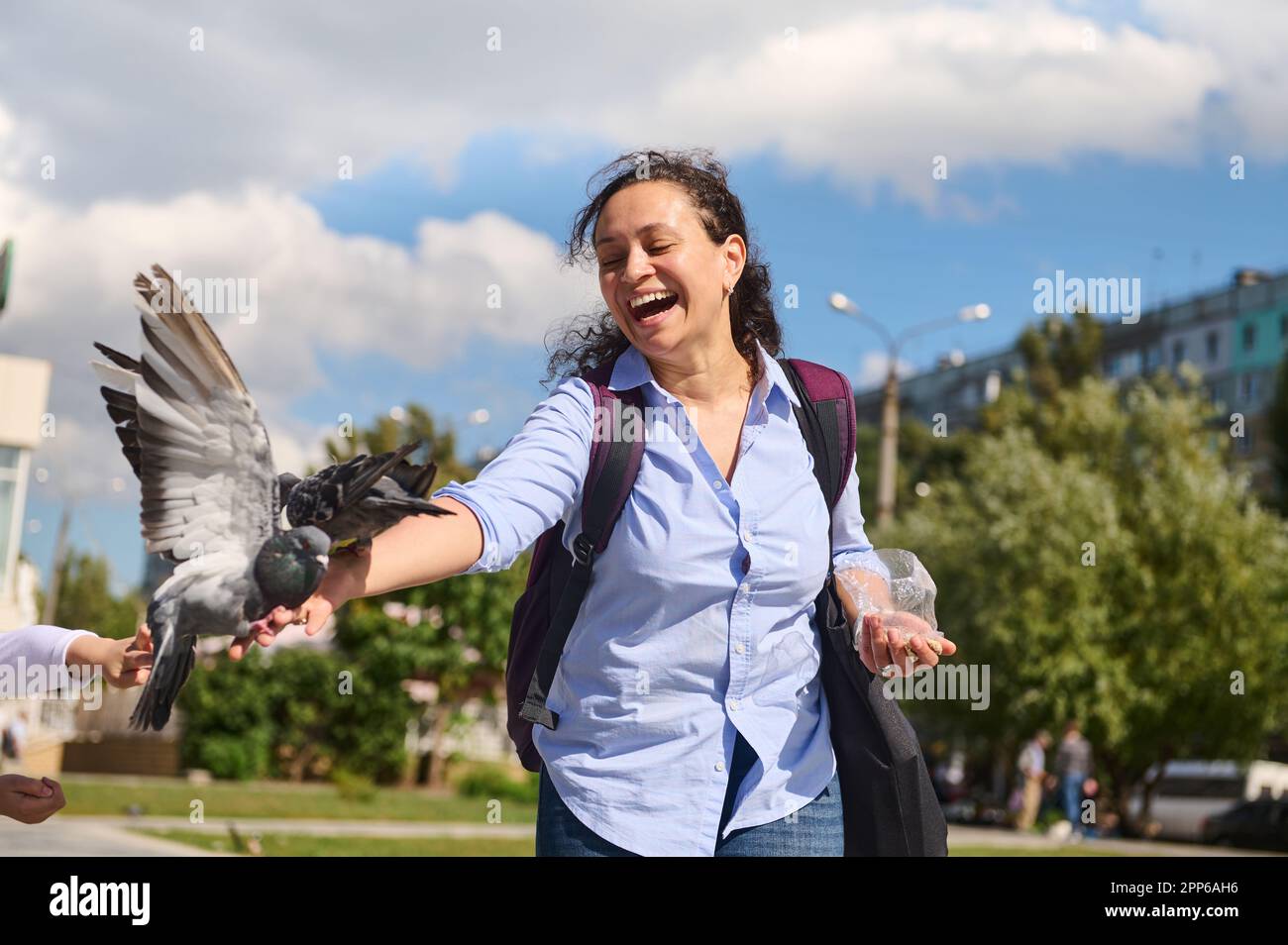 Fröhliche, positiv lächelnde, multiethnische, positive junge Frau, die an einem sonnigen Frühlingstag Tauben auf dem Platz füttert. Das Konzept von Liebe, Fürsorge und Kompassio Stockfoto