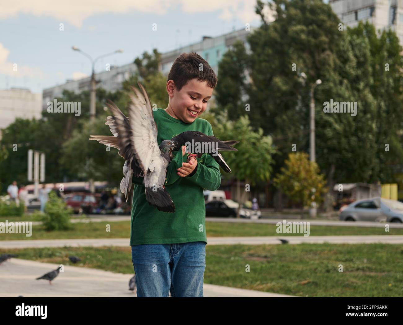 Ein glücklicher, positiv lächelnder, multiethnischer Teenager, der an einem sonnigen Frühlingstag Tauben auf dem Platz füttert. Das Konzept von Liebe, Fürsorge und Mitgefühl für die Wildnis Stockfoto