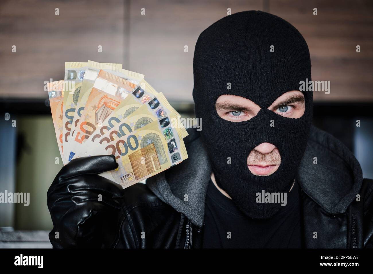 Männlicher Dieb mit Balaklava auf dem Kopf hält eine Handvoll EuroScheine vor seinen Augen. Das