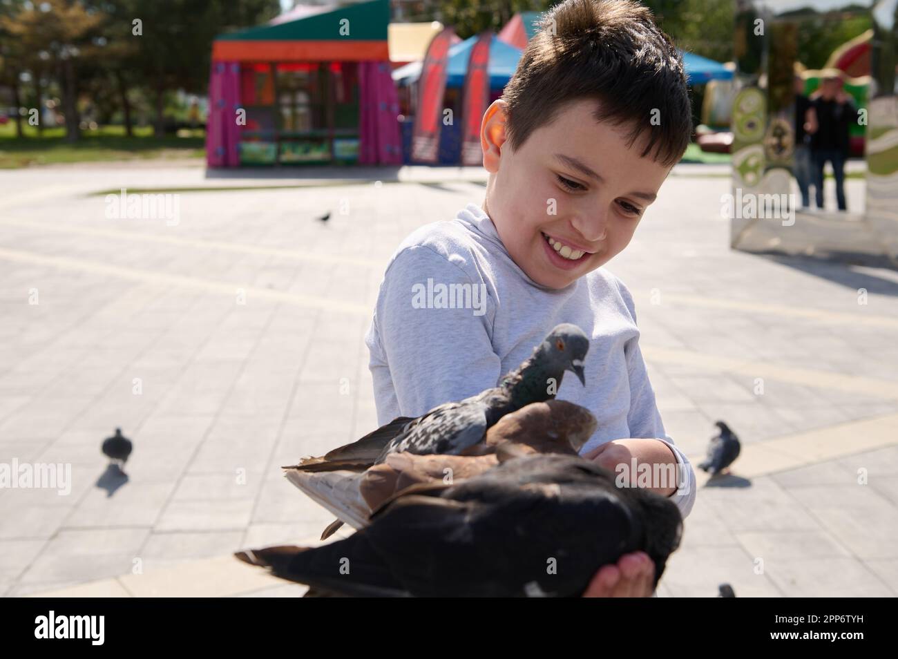 Freundlicher, fröhlicher Junge, ein liebenswertes Kind füttert Tauben im Sommerpark der Stadt. Der Begriff der Freundlichkeit und Fürsorge für Tiere. Kindheit. Kinder. Peo Stockfoto