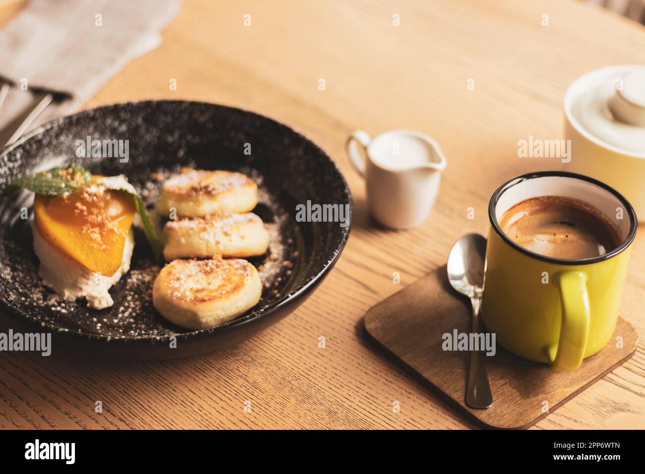 Syrniki mit Karamellbirne und Kaffeetasse. Crack-Hütten-Pfannkuchen mit Kaffee und Milch. Köstliches Frühstück. Ukrainisches Essen. Käsepfannkuchen und Kaffee. Stockfoto