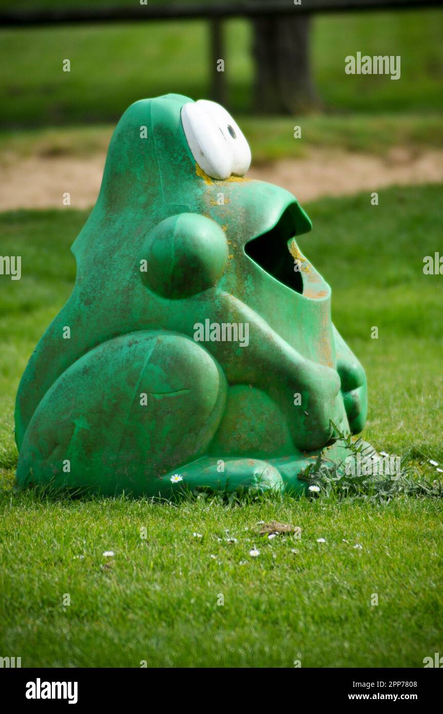 Ein gut verwitterter, komischer, grüner Frosch geformter Plastikmülleimer in einem Spielpark, England Stockfoto