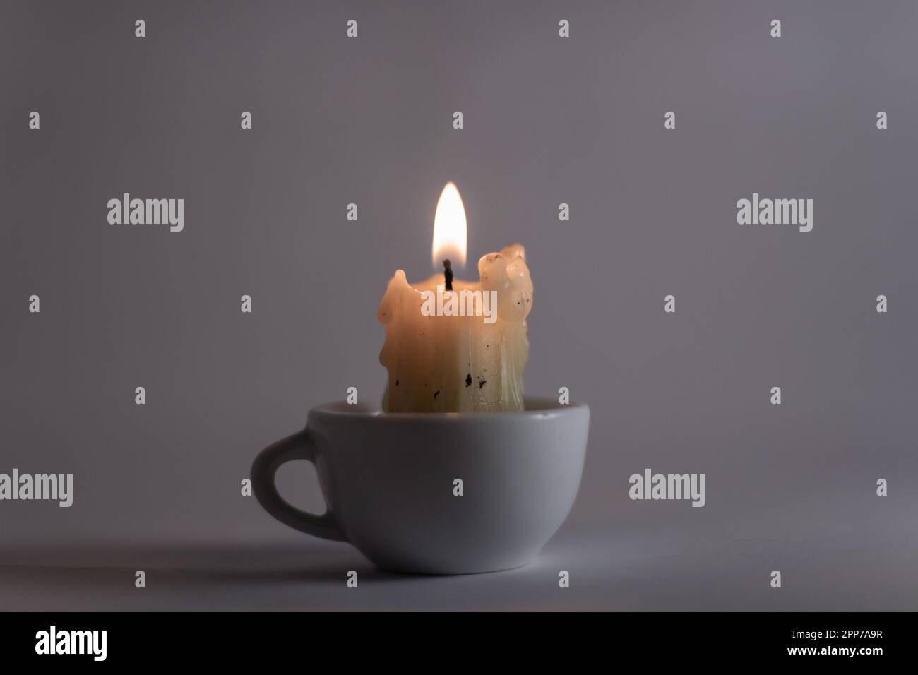 Brennende Kerze in einem weißen Becher auf weißem Hintergrund Stockfoto
