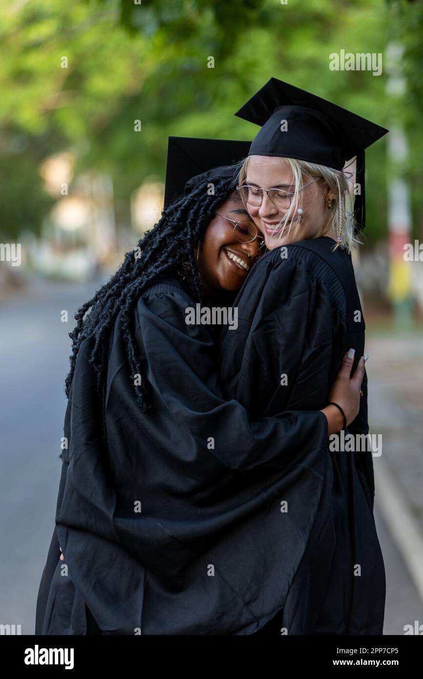 Zwei weibliche Absolventen umarmen sich nach der Abschlusszeremonie, um den Bildungserfolg und den akademischen Abschluss der Universität zu feiern. Stockfoto