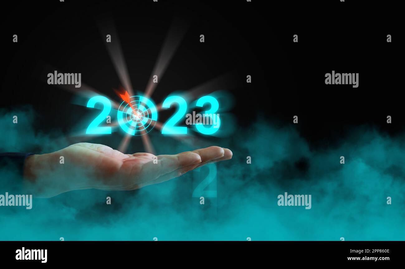 Eine Hand, die das Jahr 2023 mit einem Pfeil hält, und ein Ziel über der Wolke. Beginn des neuen Jahres, Geschäft, Projekt, Pfad, Ziel, Oder das Leben. Kontrollieren, verwalten, wählen Stockfoto