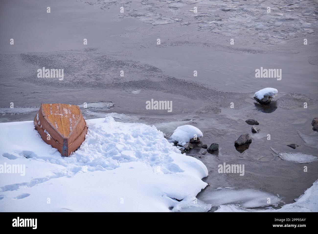 Altai Winterlandschaft mit dem Fluss Biya. Wasser fließt zwischen den schneebedeckten Ufern. Ein umgestürztes Boot liegt auf dem Eis in der Nähe der Uferseite. Stockfoto