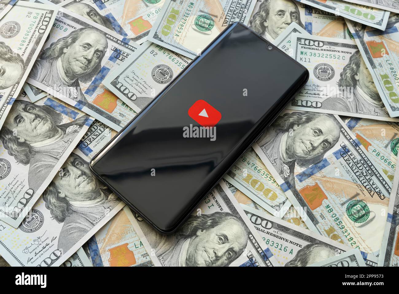 YouTube-Logo für Mobile-Video-Hosting-Anwendung auf dem Smartphone-Bildschirm und Geldhintergrund. Handy und 100-Dollar-Scheine, Draufsicht, fast Stockfoto