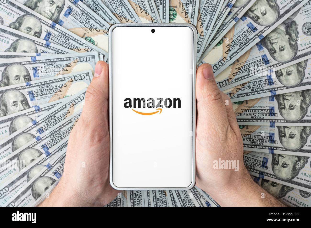 Das Logo der amazon-Website auf dem Smartphone-Bildschirm in den Händen von Männern, die auf amerikanischen Dollar liegen. 30. März 2023. Barnaul. Russland. Stockfoto