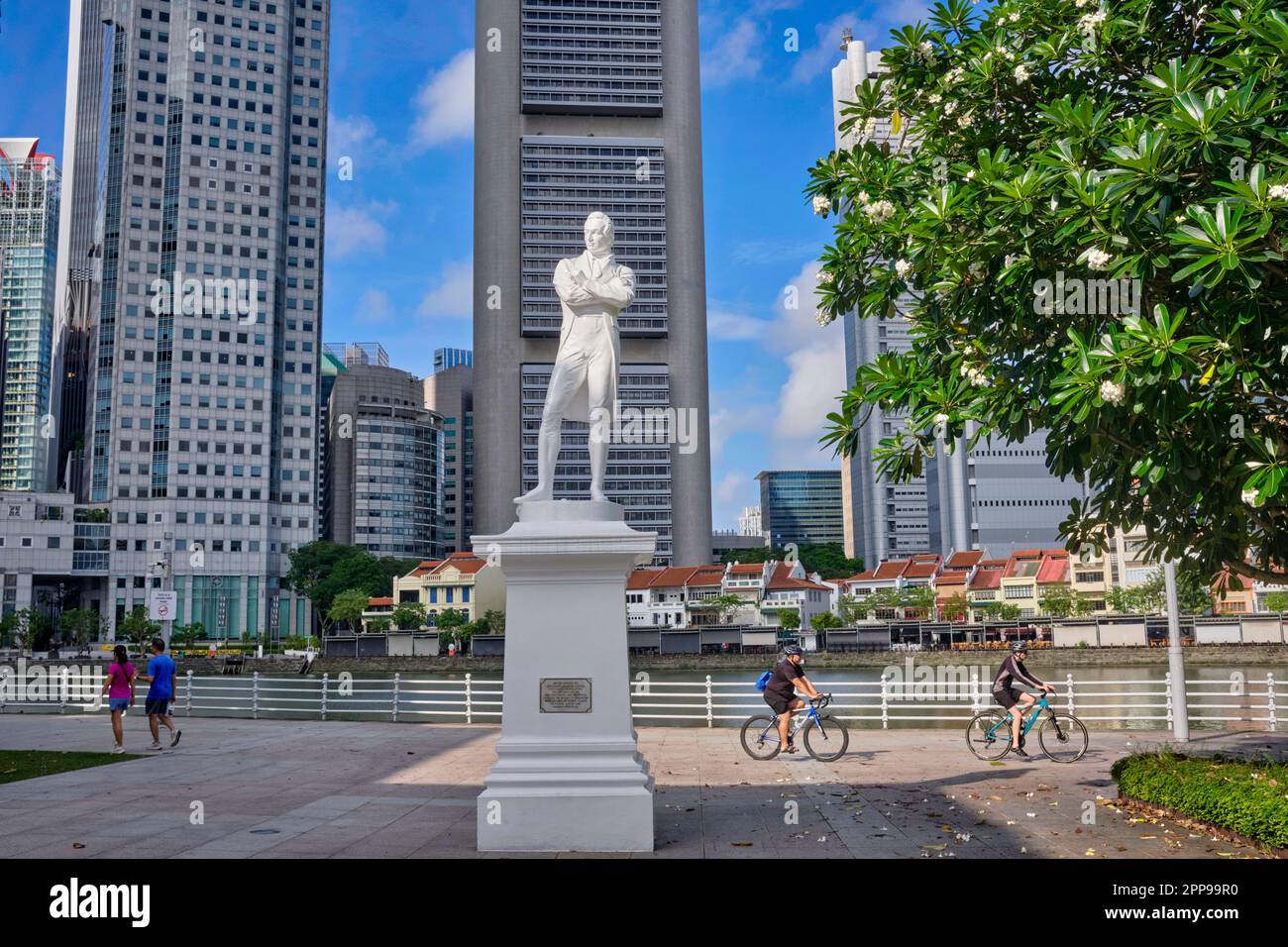 Eine Statue von Sir Stamford Raffles am Raffles Landing Pier, Boat Quay, Singapore River, Singapur; b/g: Die Skyline des Geschäftsviertels von Singapur Stockfoto