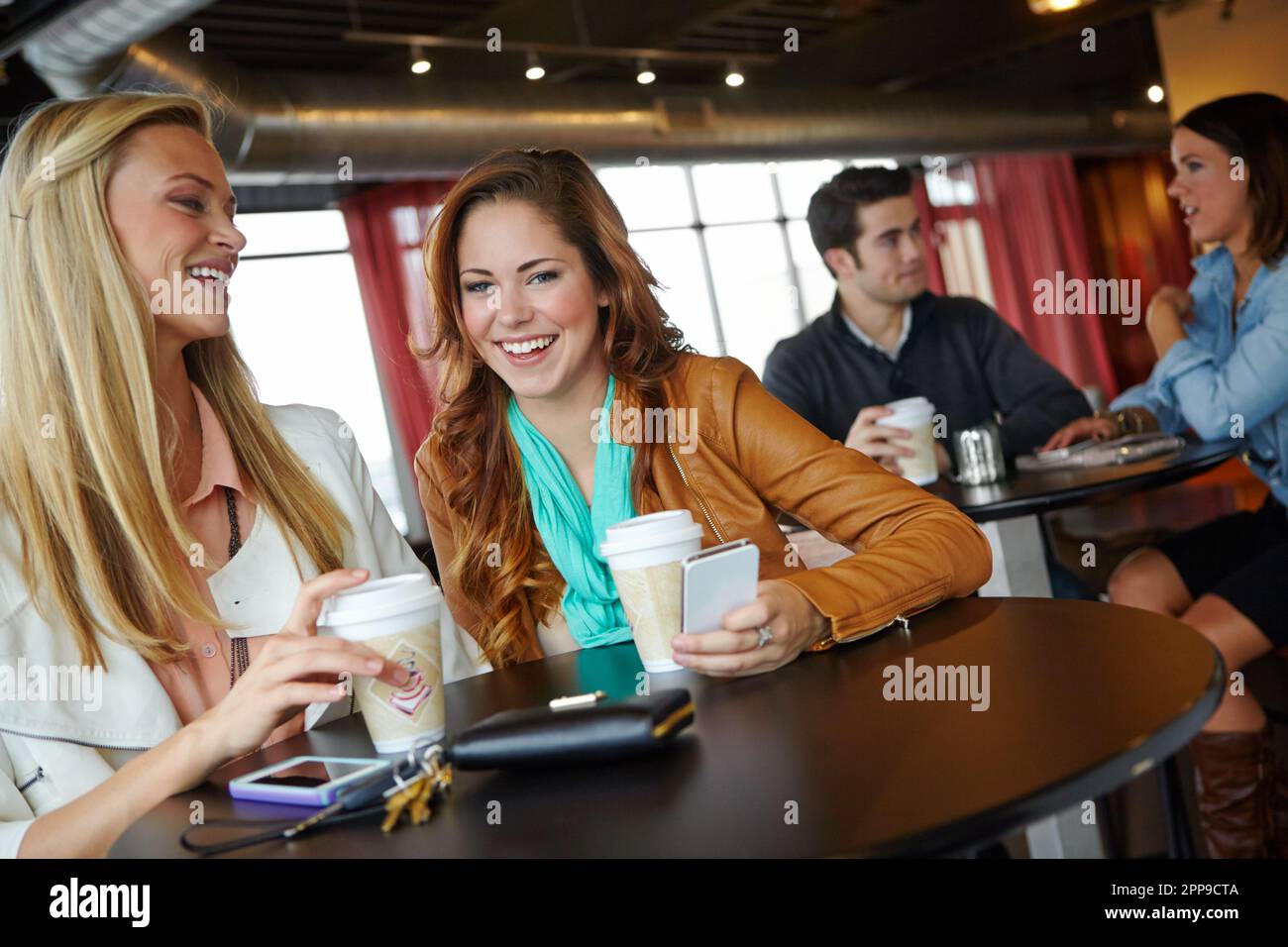 Ein kurzes Tratsch. Zwei attraktive junge Frauen, die zusammen Kaffee trinken. Stockfoto