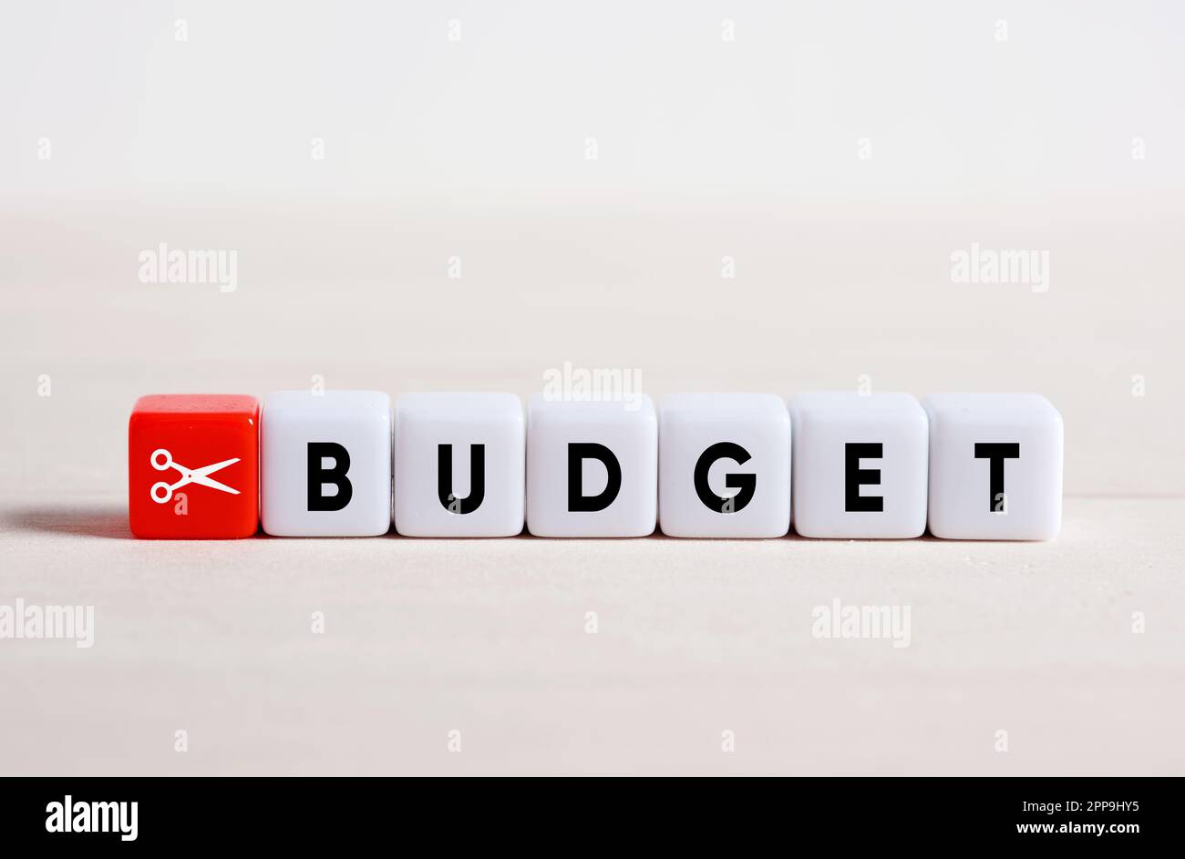 Budgetkürzungskonzept. Kostensenkung und Finanzstabilität. Kürzung des Familienbudgets. Ausgaben senken. Scheren-Symbol und das Wort Budget auf Würfeln. Stockfoto