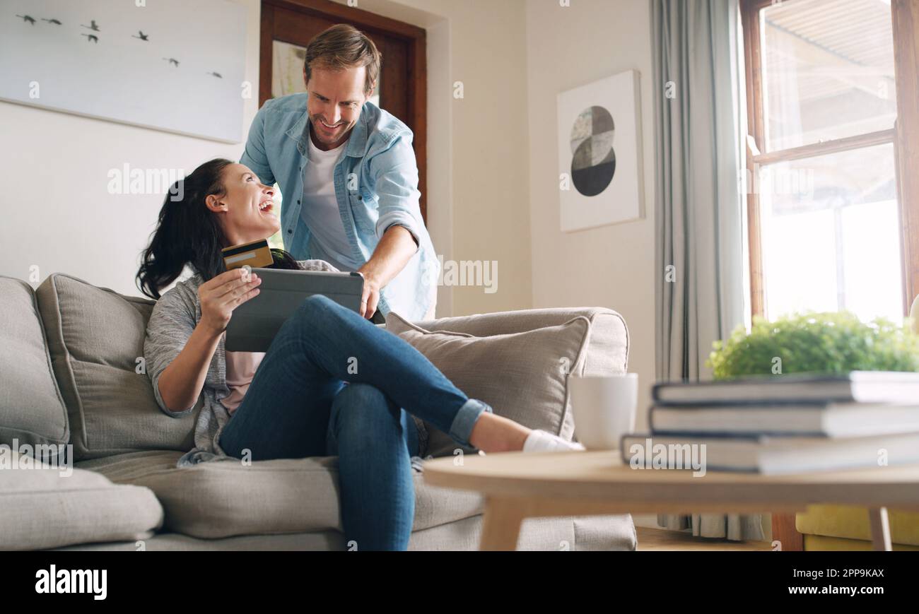 Ich wusste, dass du das wählst. Eine liebevolle junge Frau, die mit ihrem Mann lacht, während sie ein digitales Tablet zum Online-Shopping zu Hause verwendet. Stockfoto
