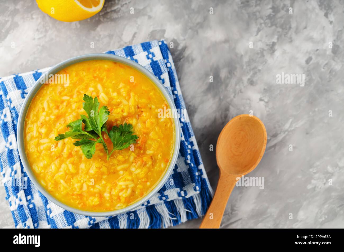 Rote Linsensuppe mit Zutaten auf grauem Hintergrund. Schüssel mit Linsensuppe und einem Holzlöffel auf einer Leinenserviette. Draufsicht Stockfoto