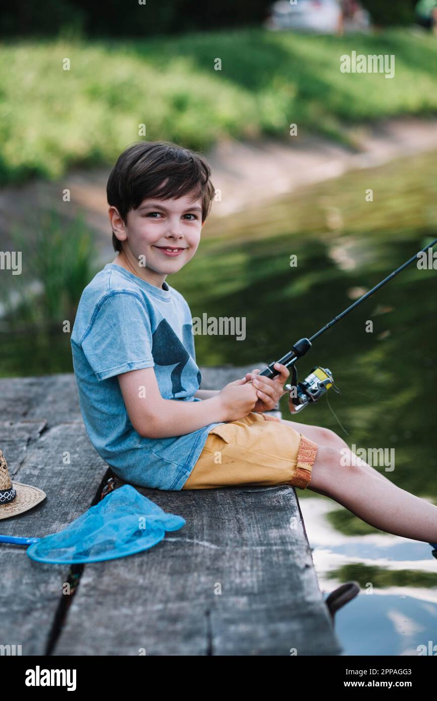 Glücklicher Junge sitzt hölzernen Pier See hält Angelrute Stockfoto