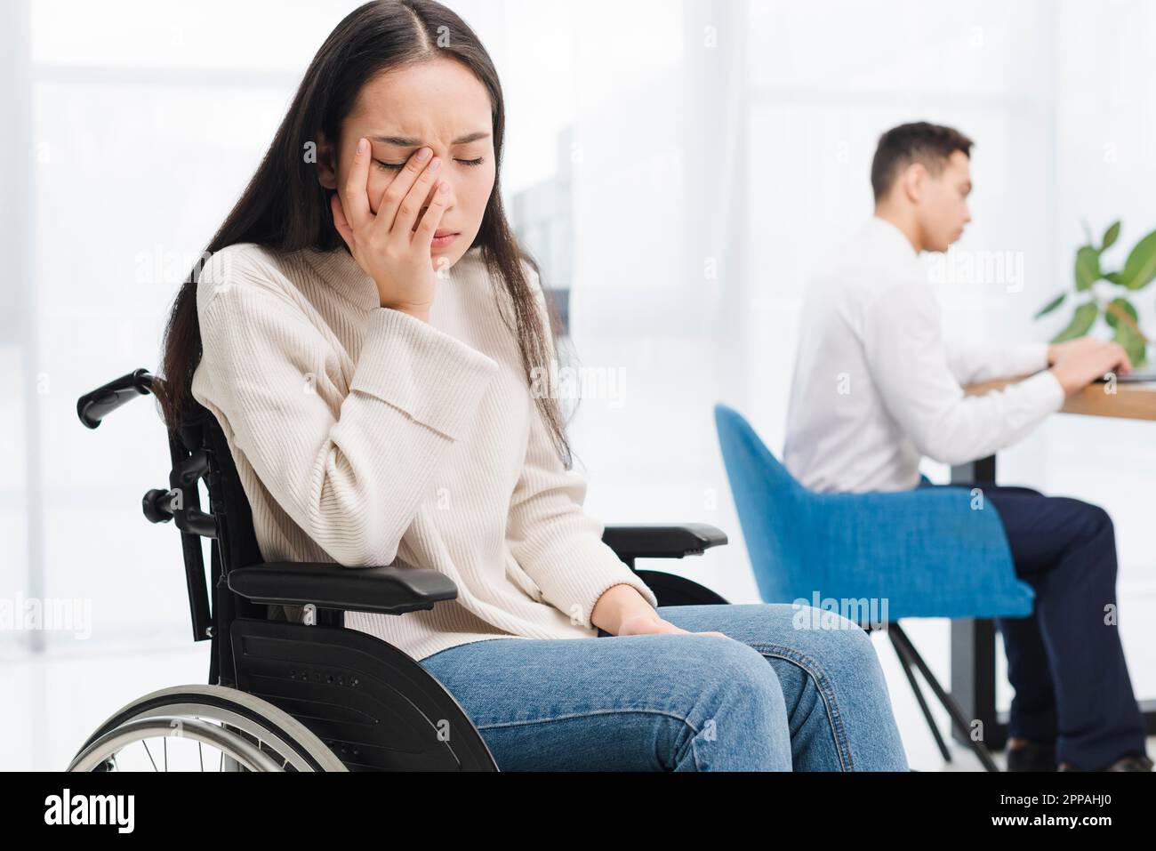 Besorgt junge Frau sitzt Rollstuhl sitzen vor männlichen Kollegen mit Laptop Stockfoto