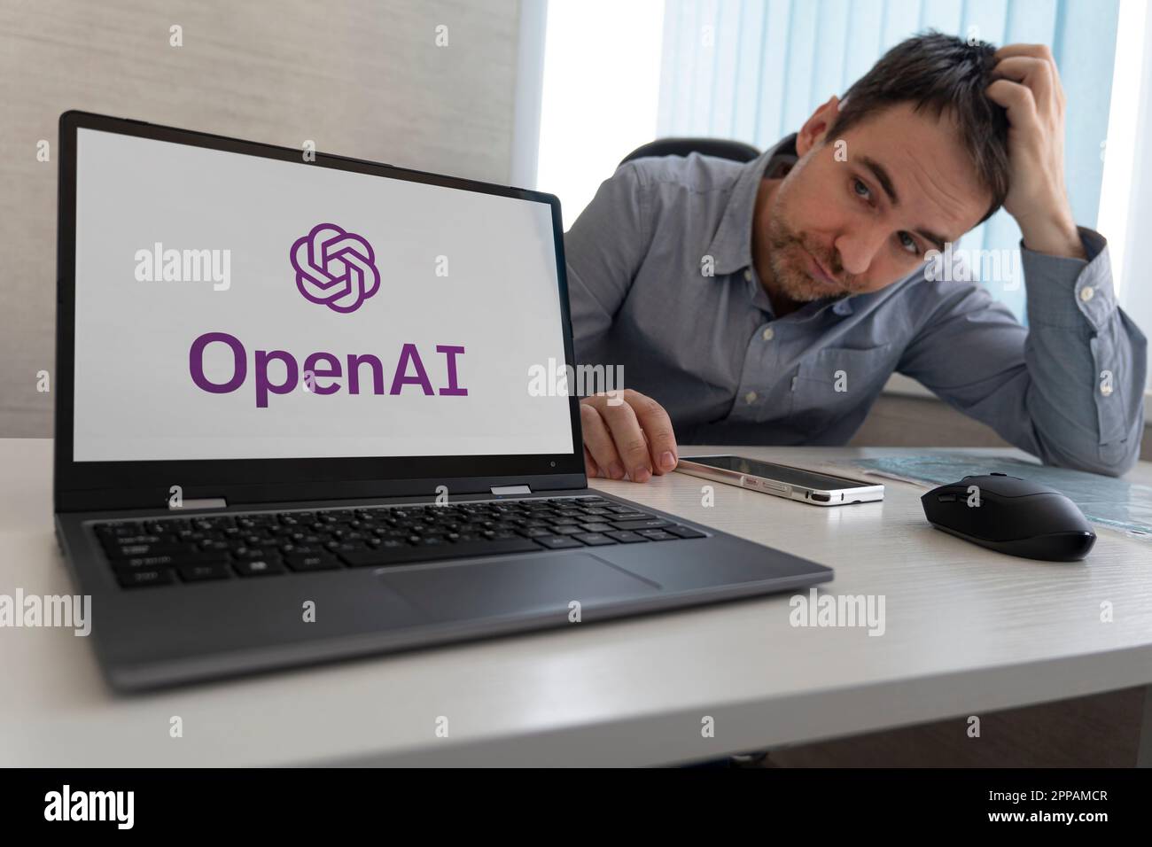 Einen Menschen durch künstliche Intelligenz ersetzen. Konzept. OpenAI-Logo auf dem Laptop-Bildschirm neben einem traurigen Mitarbeiter, der am Arbeitsplatz sitzt. Barnaul. R Stockfoto