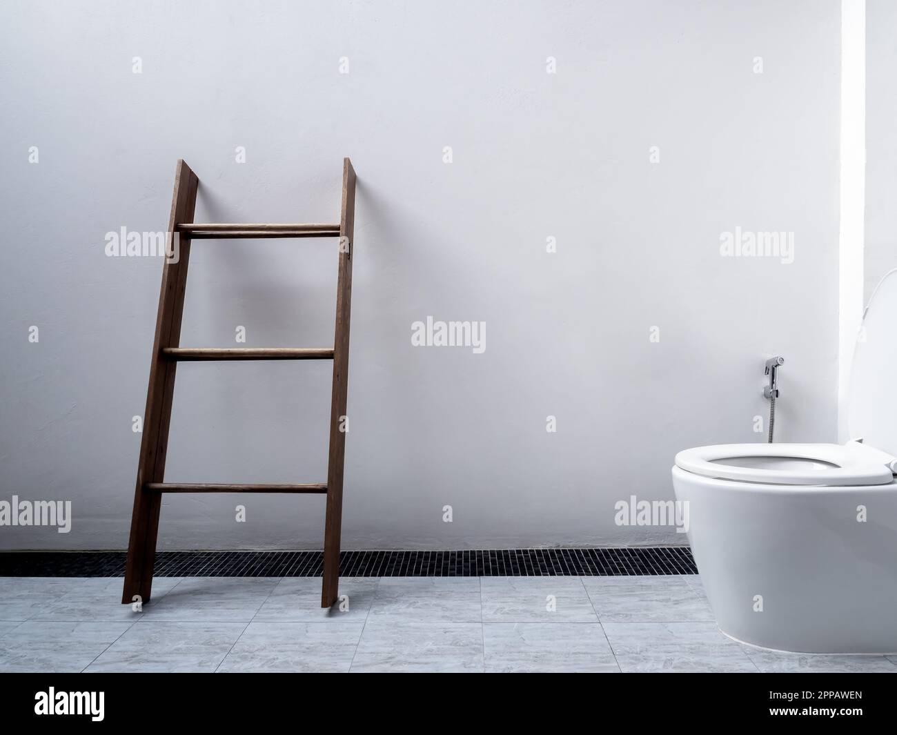 Weiße Toiletteneinrichtung, minimalistischer Stil. Handtuchhalter aus Holz, dunkelbraune Stehleiter für Handtücher in der Nähe der Toilette mit Keramikspülung und Bidet-Dusche auf dem Platz Stockfoto