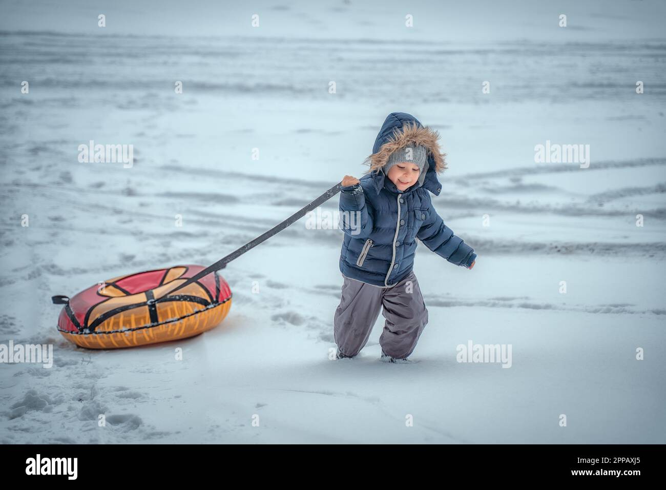 Ein kleiner Junge zieht einen aufblasbaren Schlauch. Süßer Junge mit Schneerohr. Winterferien. Winterski den Berg hinunter. Stockfoto