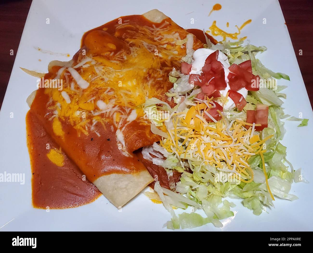 Enchilada mit Rindfleisch und Huhn mit Salat und saurer Sahne auf einer weißen Keramikplatte Stockfoto