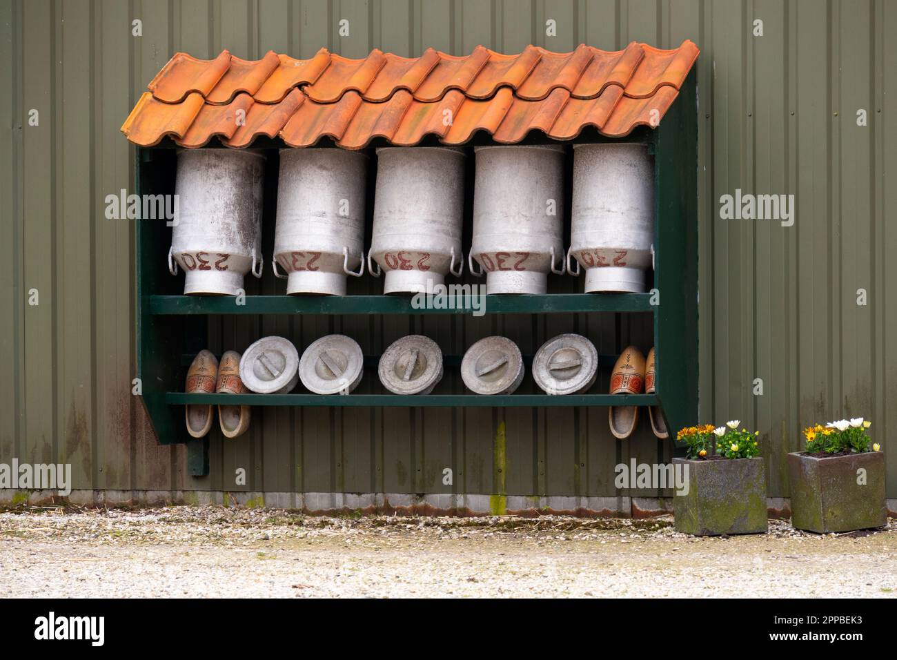 Typisches holländisches Bild leerer traditioneller Milchbehälter und Holzschuhe unter einem gefliesten Dach Stockfoto