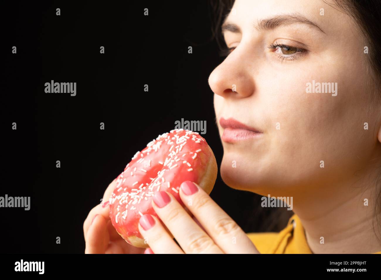 Eine Frau beißt einen großen roten Donut, einen schwarzen Hintergrund, ein Ort für Text. Gluttonie, überfressen und zuckersüchtig. Stockfoto