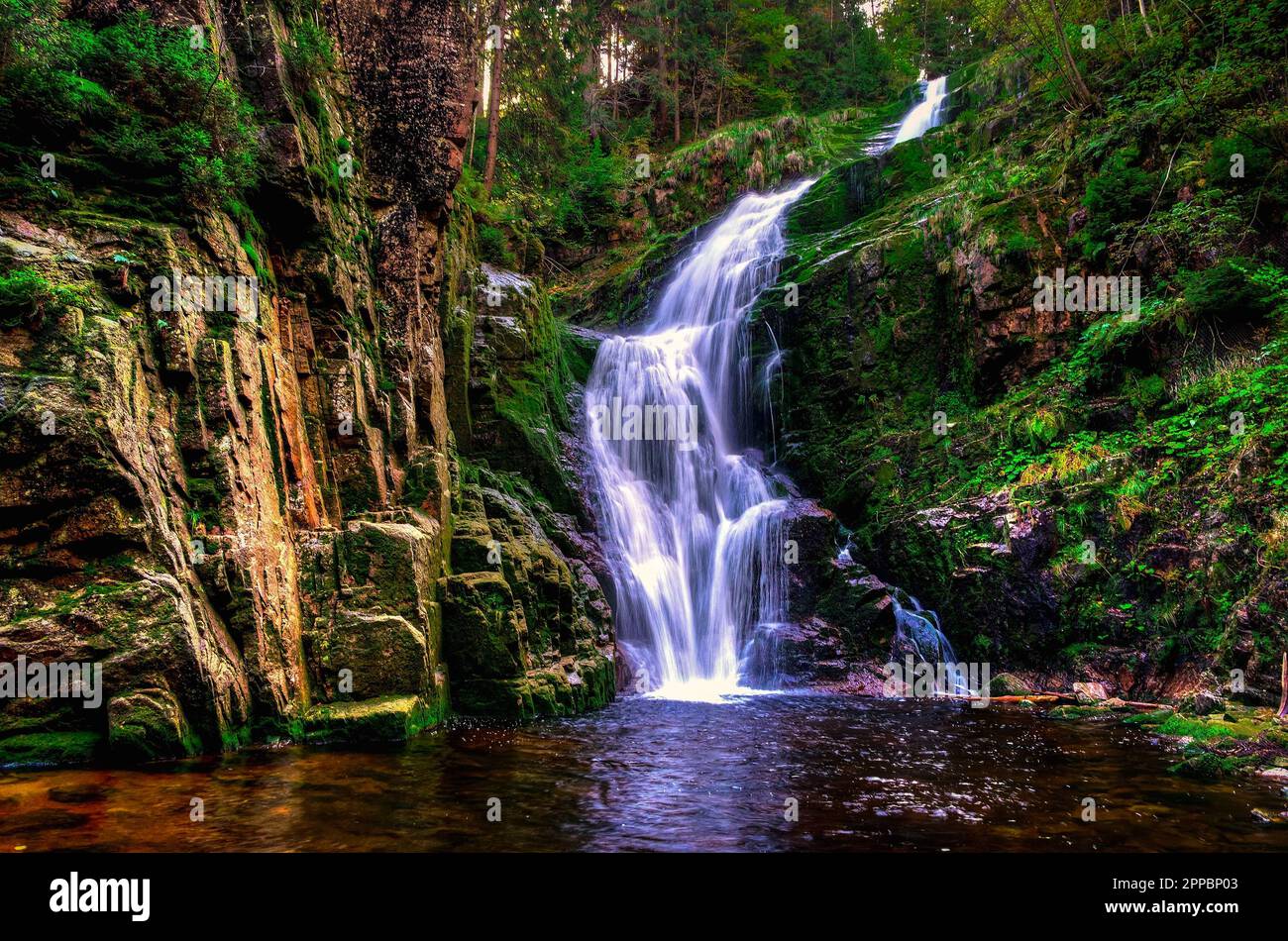 Bezaubernder Wasserfall in den Bergen zwischen Felsen und grünen Pflanzen. Der berühmte Kamienczyk-Wasserfall im Karkonosze-Nationalpark, Polen. Stockfoto