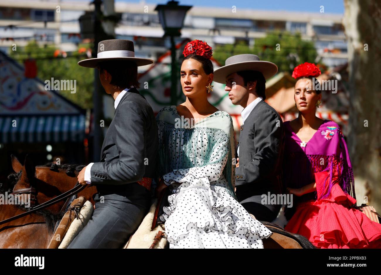 Andalusische Reiter und Frauen, die flamenca-Kleider tragen, reiten ...
