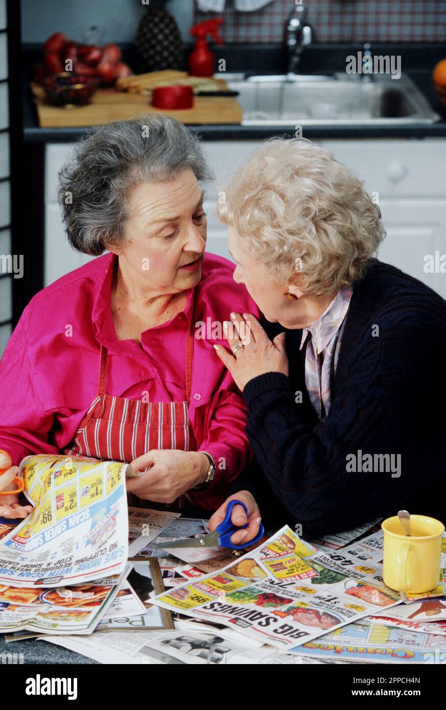 Zwei weibliche Seniorenfreunde, die Gutscheine in der Küche ausschneiden Stockfoto