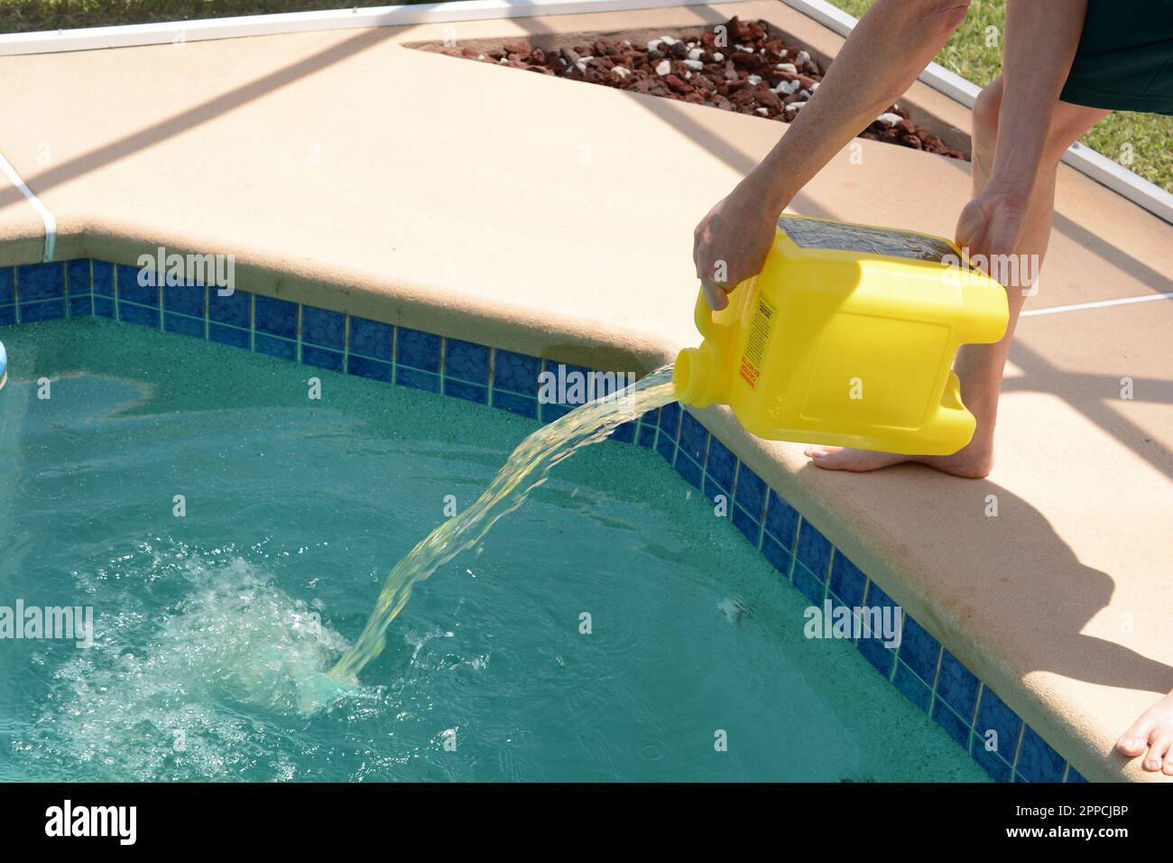 Mann, der Chlor zur Wartung in den Swimmingpool gießt. Flüssigkeitsstrom, der über die Wasseroberfläche spritzt Stockfoto
