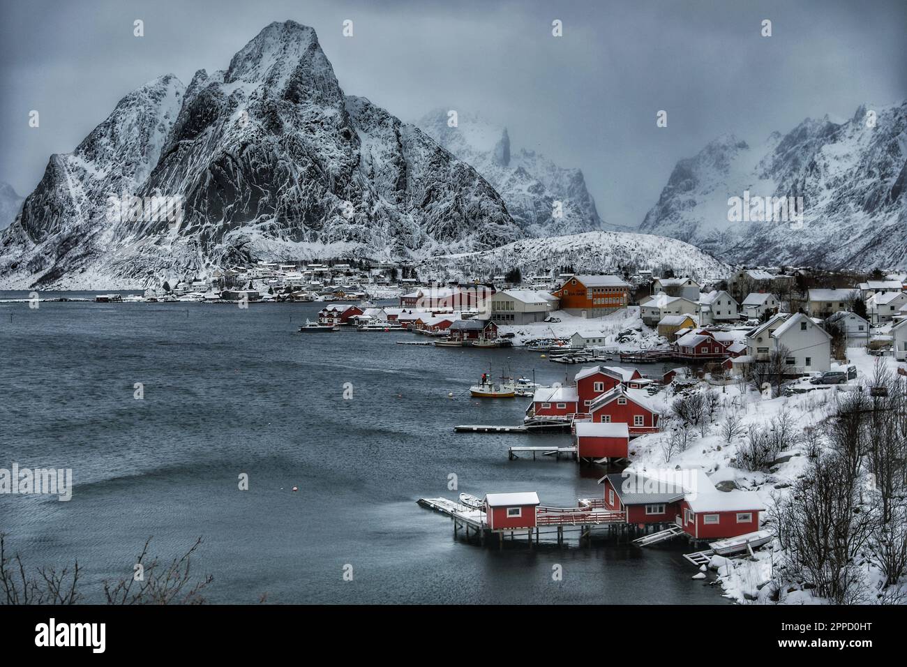 Majestätische schneebedeckte Berge umgeben eine malerische Bucht mit mehreren kleinen Booten und größeren Booten, die eine atemberaubende Landschaft schaffen Stockfoto