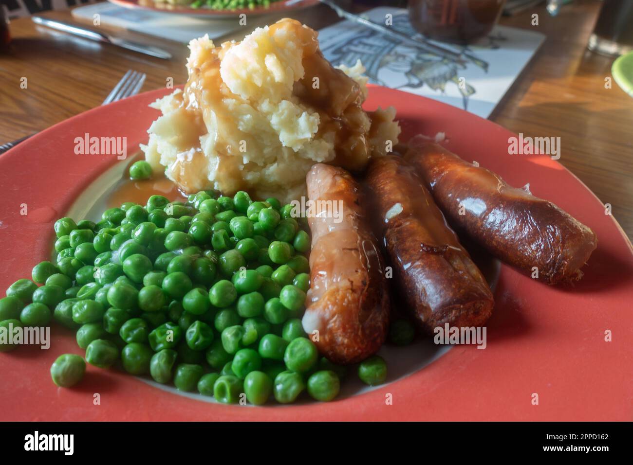 Würstchen, Kartoffelpüree und Erbsen auf einem roten Teller, Trostessen zum Abendessen. Stockfoto