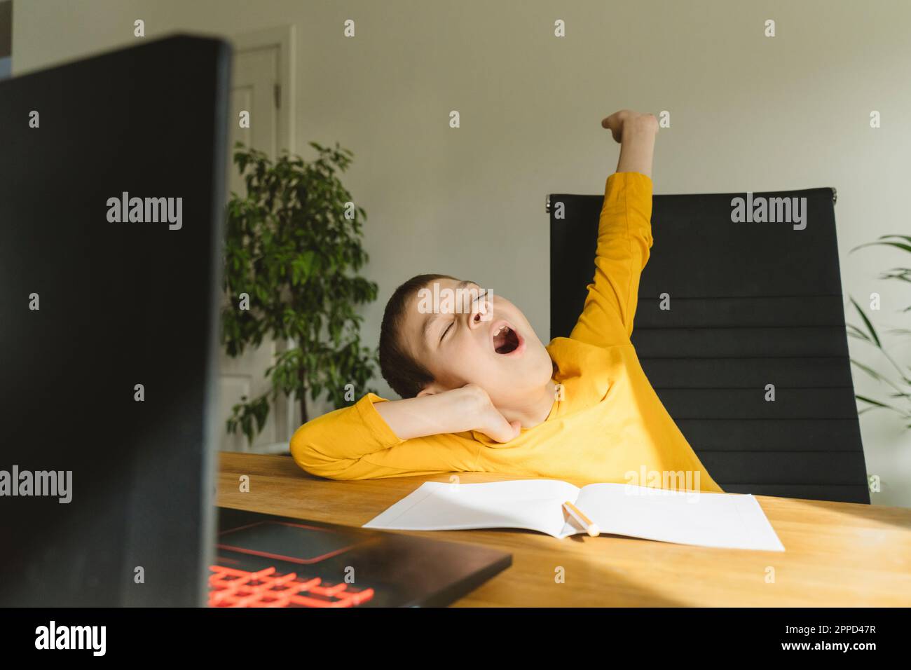 Müder Junge, der zu Hause am Tisch gähnt Stockfoto