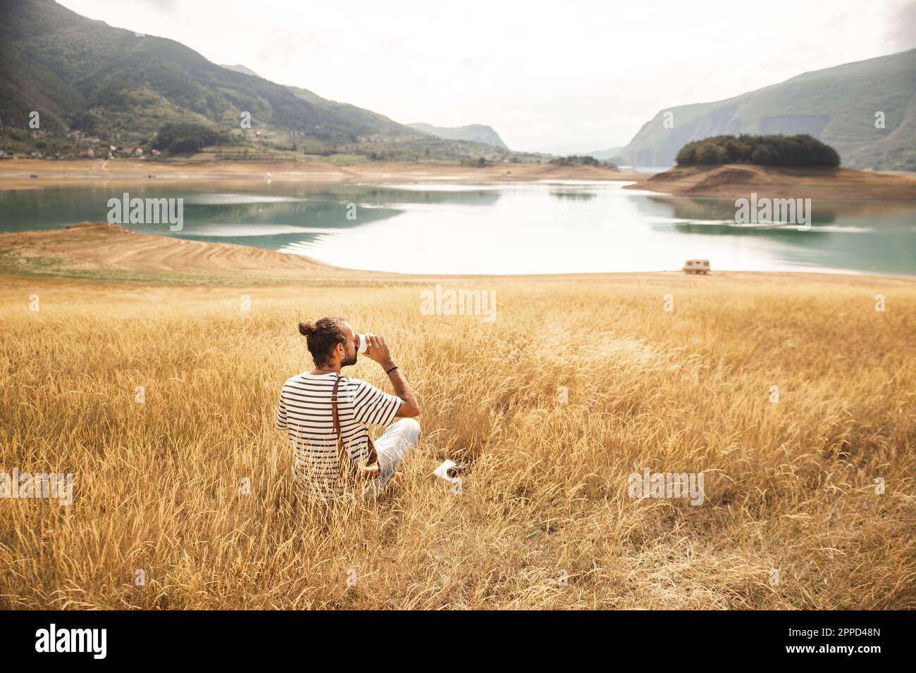 Ein Mann, der Kaffee trinkt und vor dem Rama Lake sitzt Stockfoto