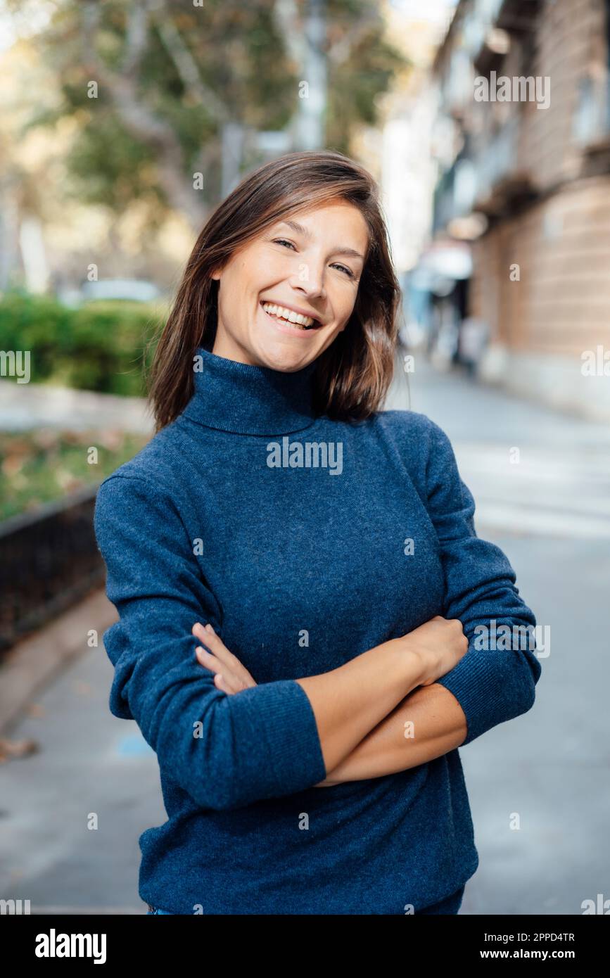 Glückliche Frau mit gekreuzten Armen, die auf dem Fußweg steht Stockfoto