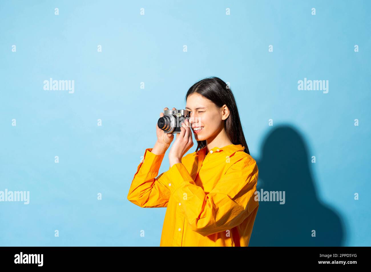 Junge Frau, die vor einem farbigen Hintergrund ein Foto durch die Kamera klickt Stockfoto