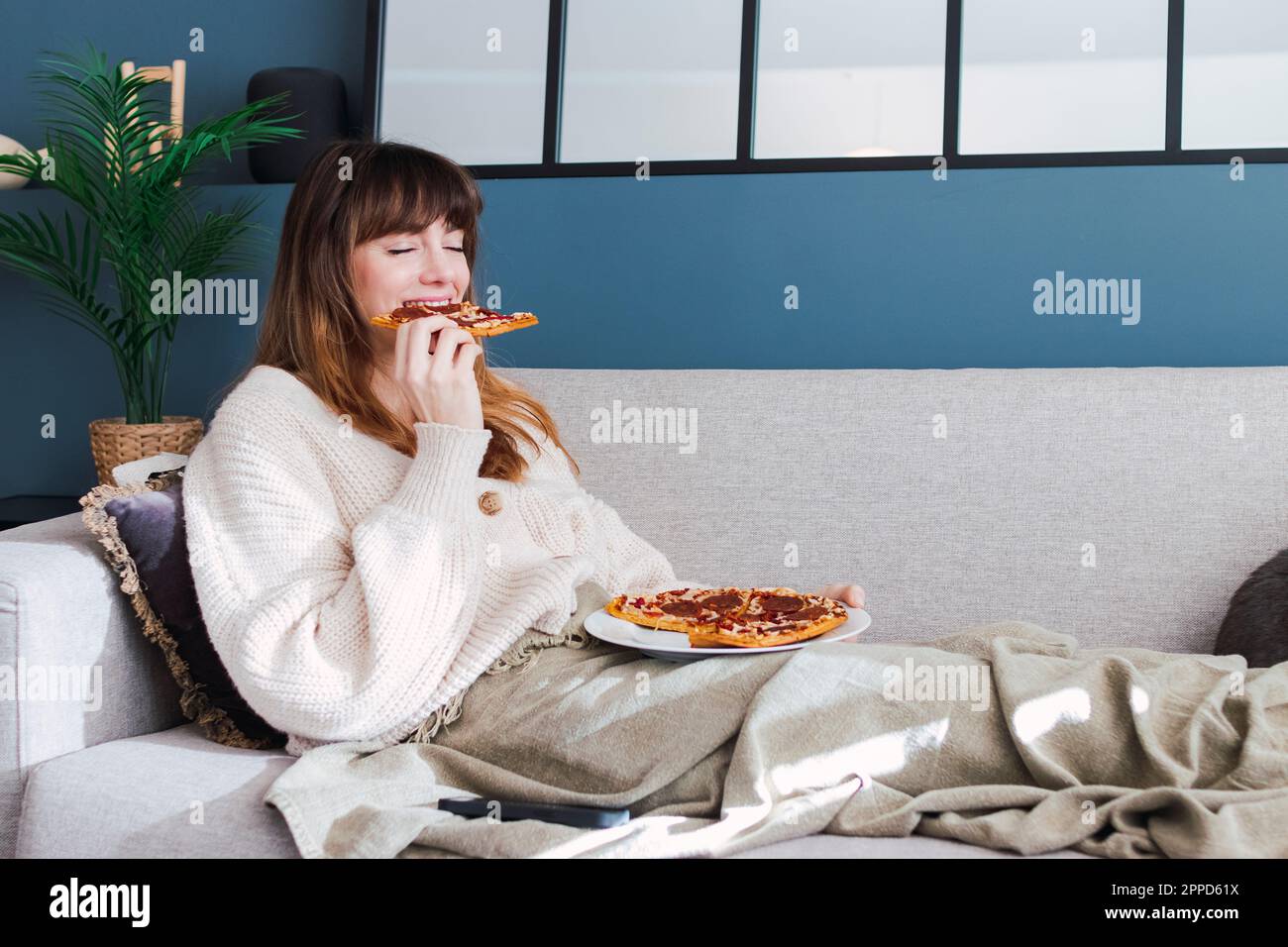 Eine Frau, die zu Hause Pizza auf dem Sofa genießt Stockfoto