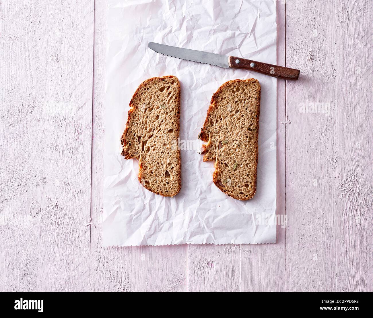 Studioaufnahme von zwei Scheiben Brot und Küchenmesser, die auf einem Stück Papier liegen Stockfoto