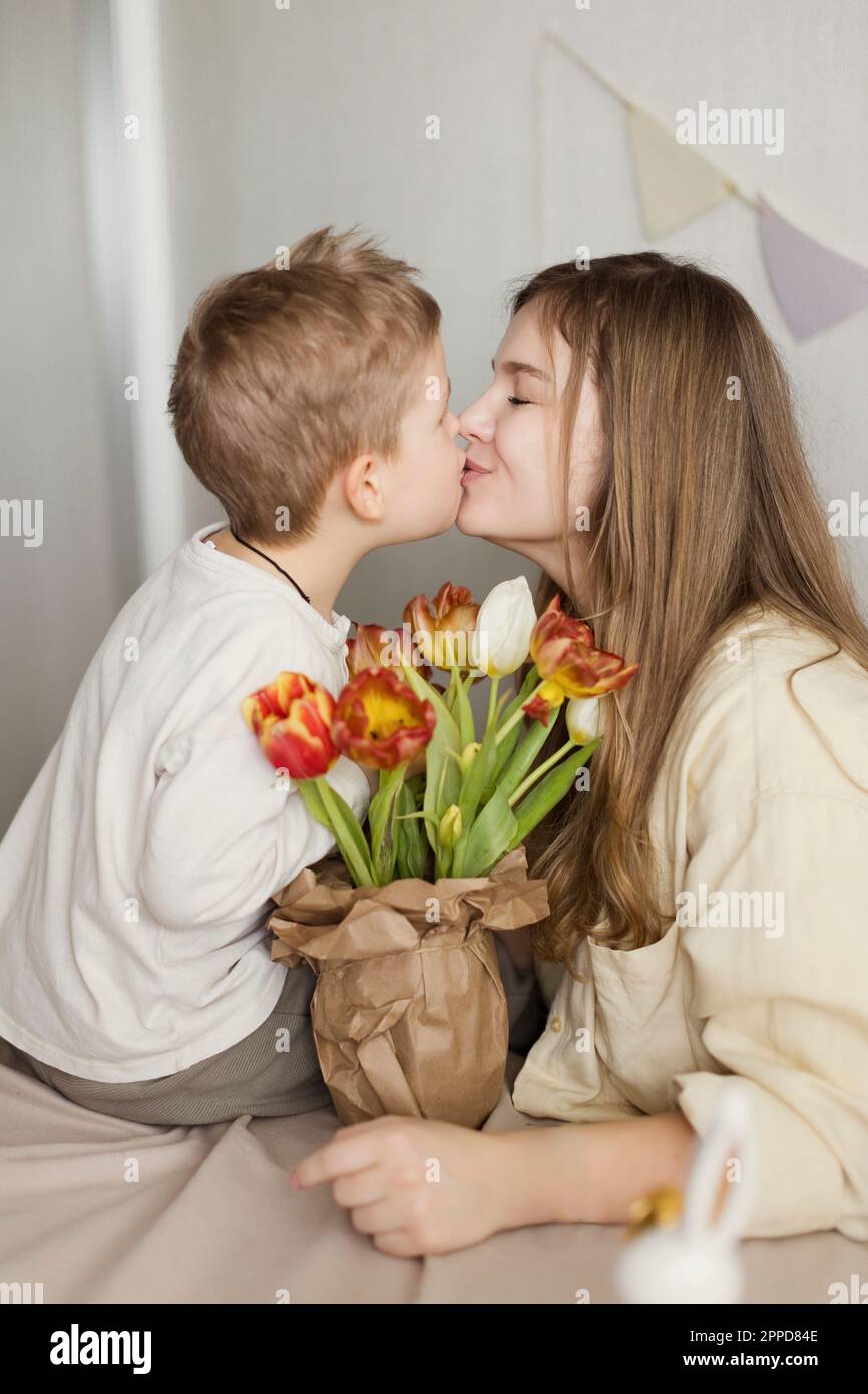 Sohn küsst Mutter zu Hause mit Tulpenstrauß Stockfoto