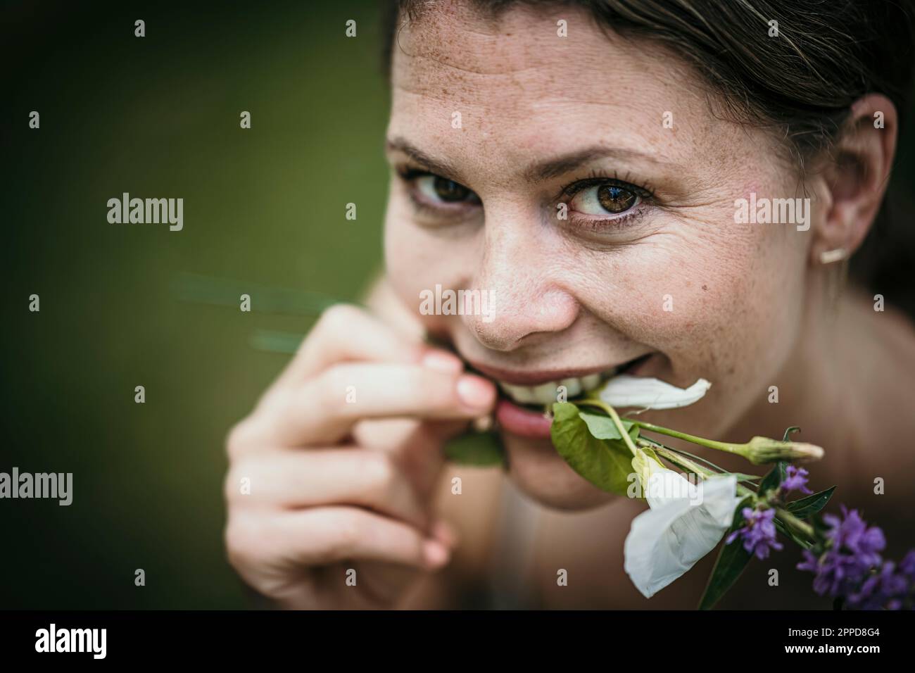 Lächelnde Frau, die Blumen im Mund hält Stockfoto