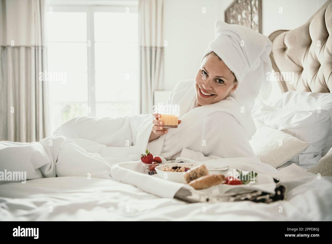 Glückliche Frau, die zu Hause ein Saftglas am Frühstückstablett im Bett hielt Stockfoto