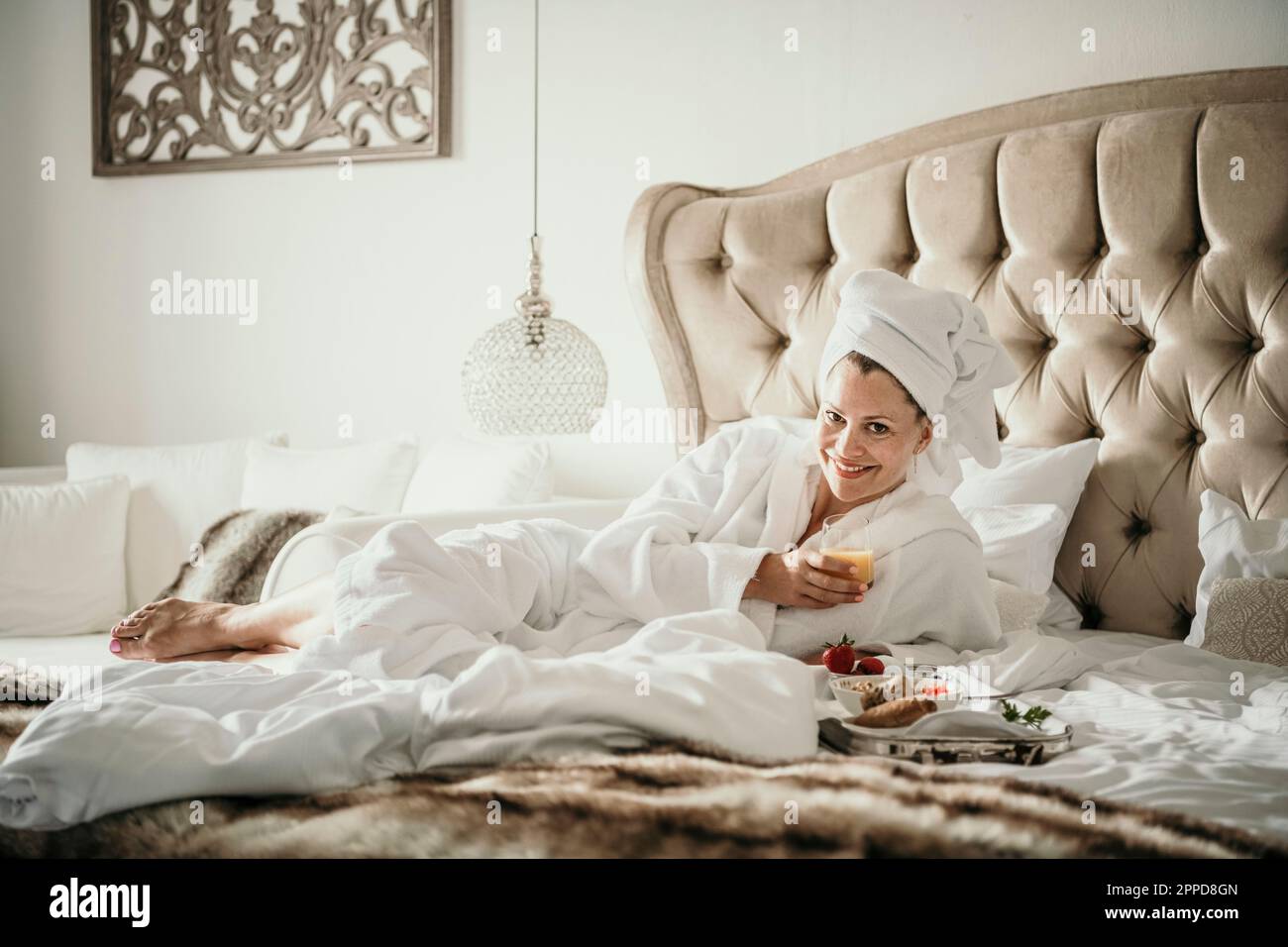 Glückliche Frau im Bademantel, die das Frühstück zu Hause im Bett genießt Stockfoto