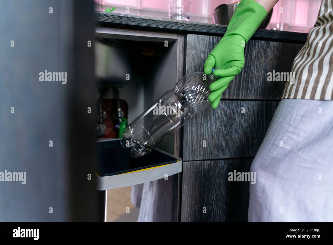 Eine Frau mit Handschuhen, die zu Hause Plastikflaschen in den Mülleimer wirft Stockfoto