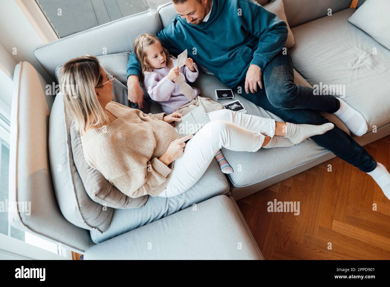 Tochter schaut sich Ultraschallbilder an, während sie im Wohnzimmer von Eltern sitzt Stockfoto