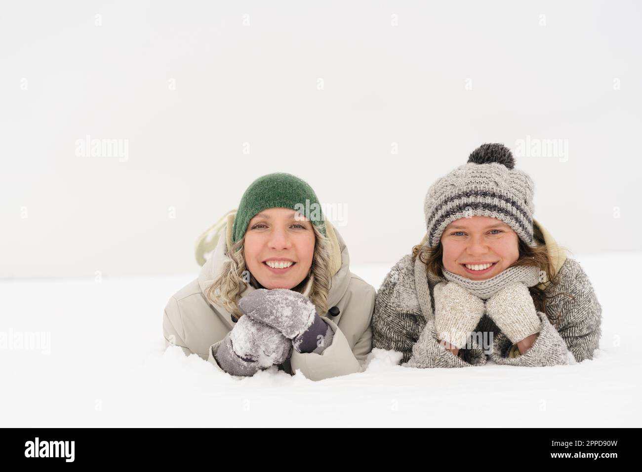 Glückliche Freunde, die Strickmützen und Handschuhe tragen, die auf dem Schnee liegen Stockfoto