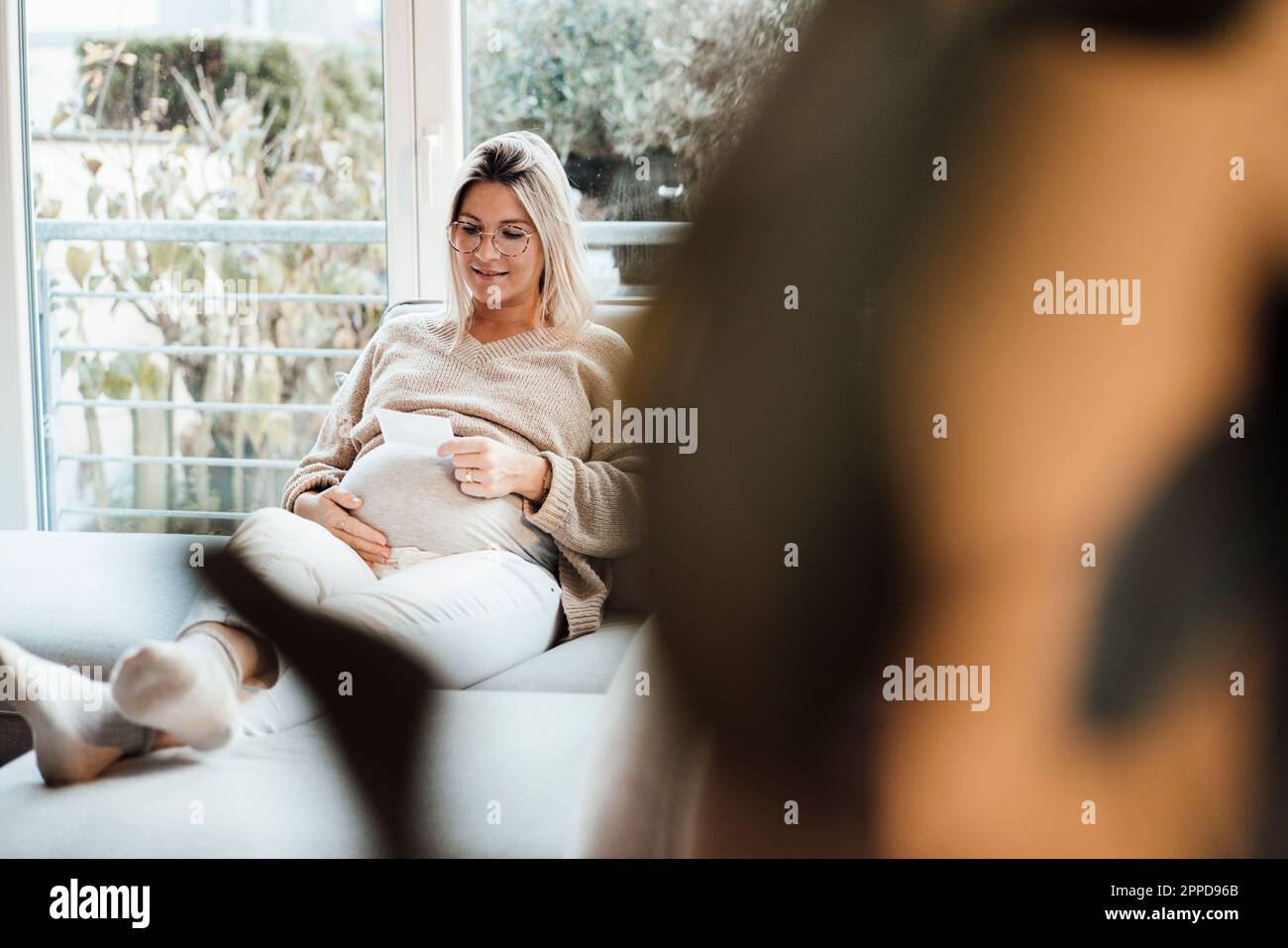 Lächelnde Frau, die zu Hause Ultraschallfotos ansieht Stockfoto