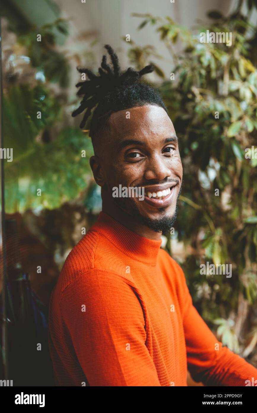 Glücklicher junger Mann, der neben der Pflanze sitzt Stockfoto